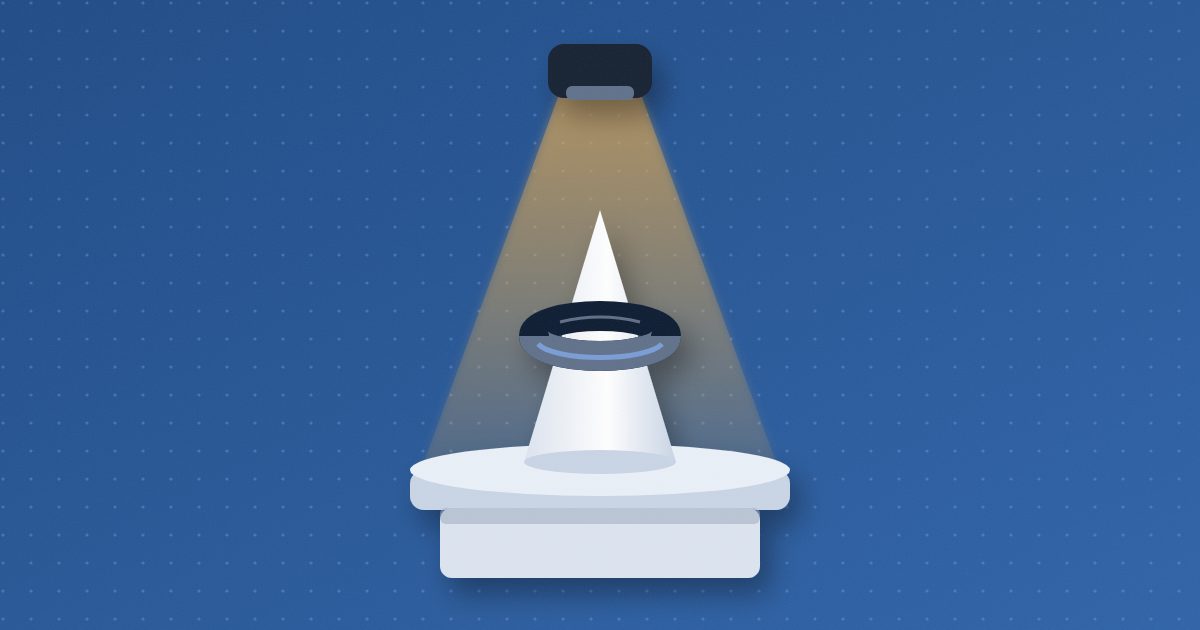A thick ring rests on a cone-shaped jewelry stand atop a round pedestal, lit from above by an amber spotlight beam.