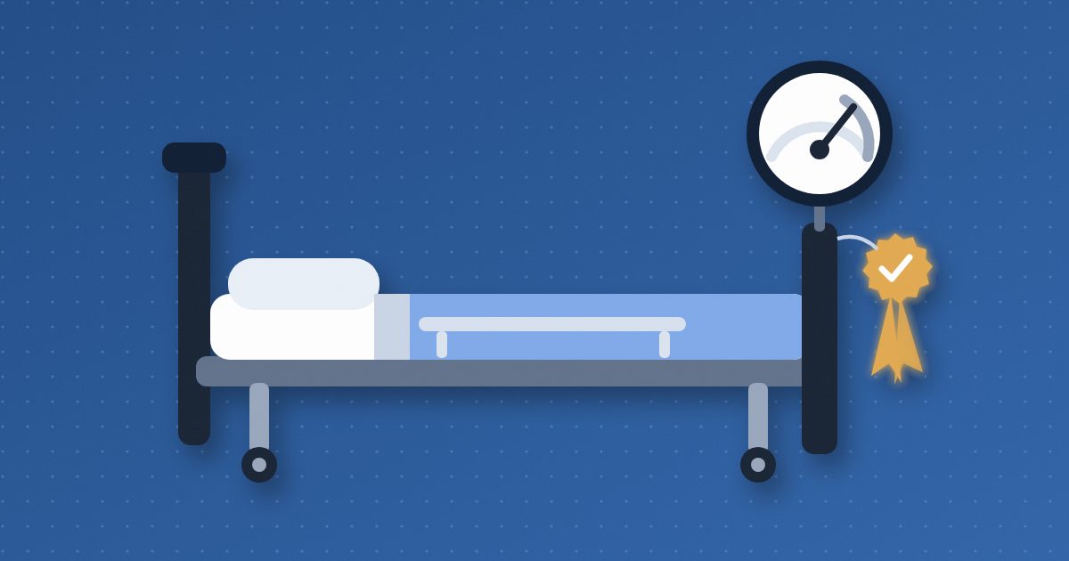A hospital bed with a round dial gauge mounted above its footboard and a glowing amber approval rosette with a check mark hanging beside it.