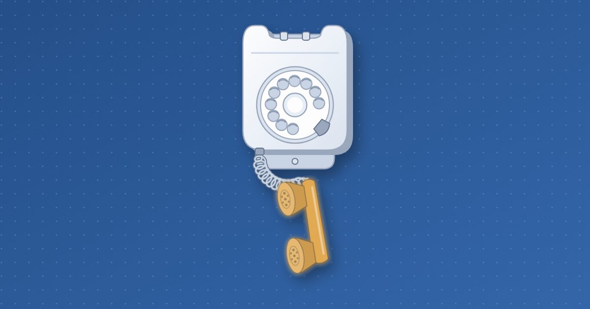 An old wall telephone with a blank rotary dial and an empty cradle, its amber handset hanging below by a coiled cord.
