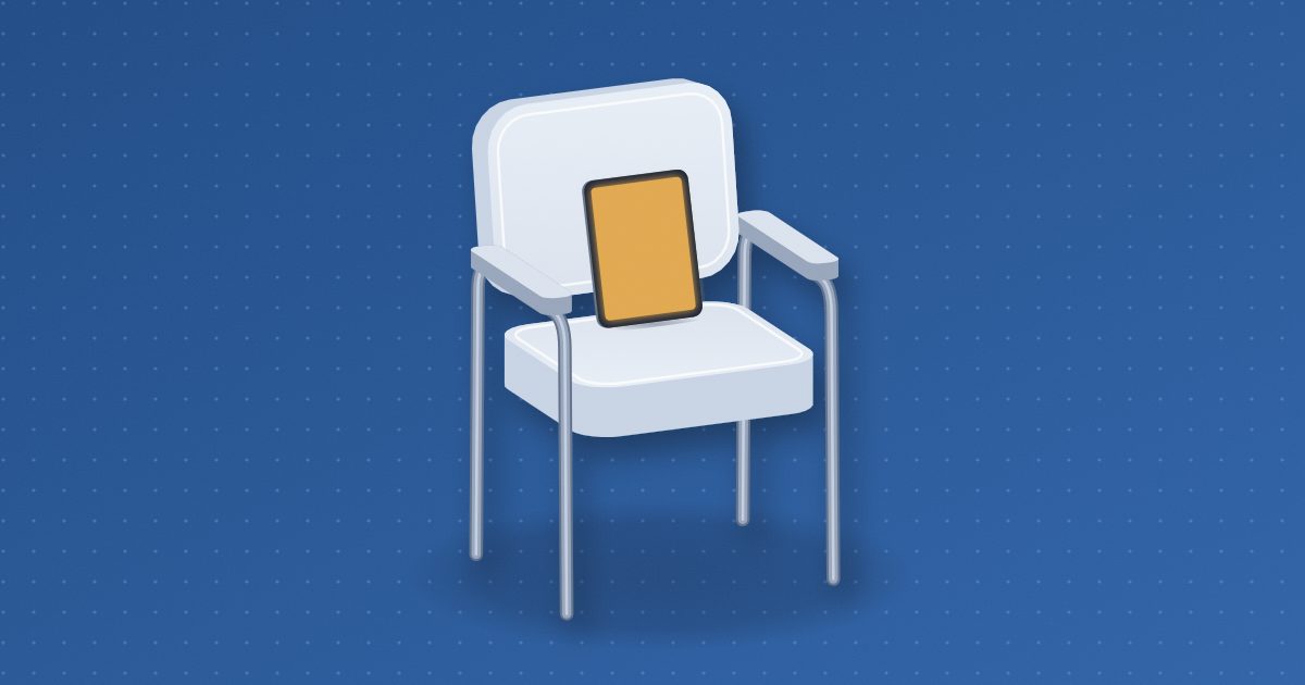 A padded exam-room side chair with metal legs and armrests, a tablet standing on its seat and leaning against its back, the blank screen glowing amber.