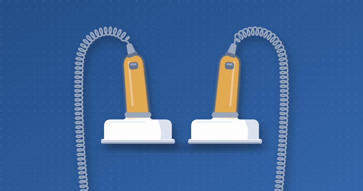 Two defibrillator paddles standing side by side on flat metal electrode plates, with amber handles and coiled cords looping off the bottom of the frame.