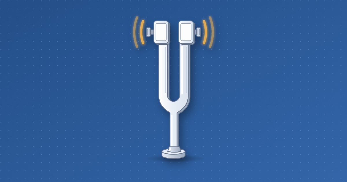 A tuning fork with clamp-on weights on its tines, standing upright on its round foot, with two pairs of short amber arcs beside the tines showing vibration.